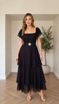 Front view of black tiered square neck maxi dress with floral buckle belt
