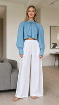 Front view of model wearing dusty blue cropped pleated long sleeve shirt with white trousers