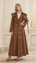 Full-length front view of woman wearing brown maxi belted trench coat with gold hardware