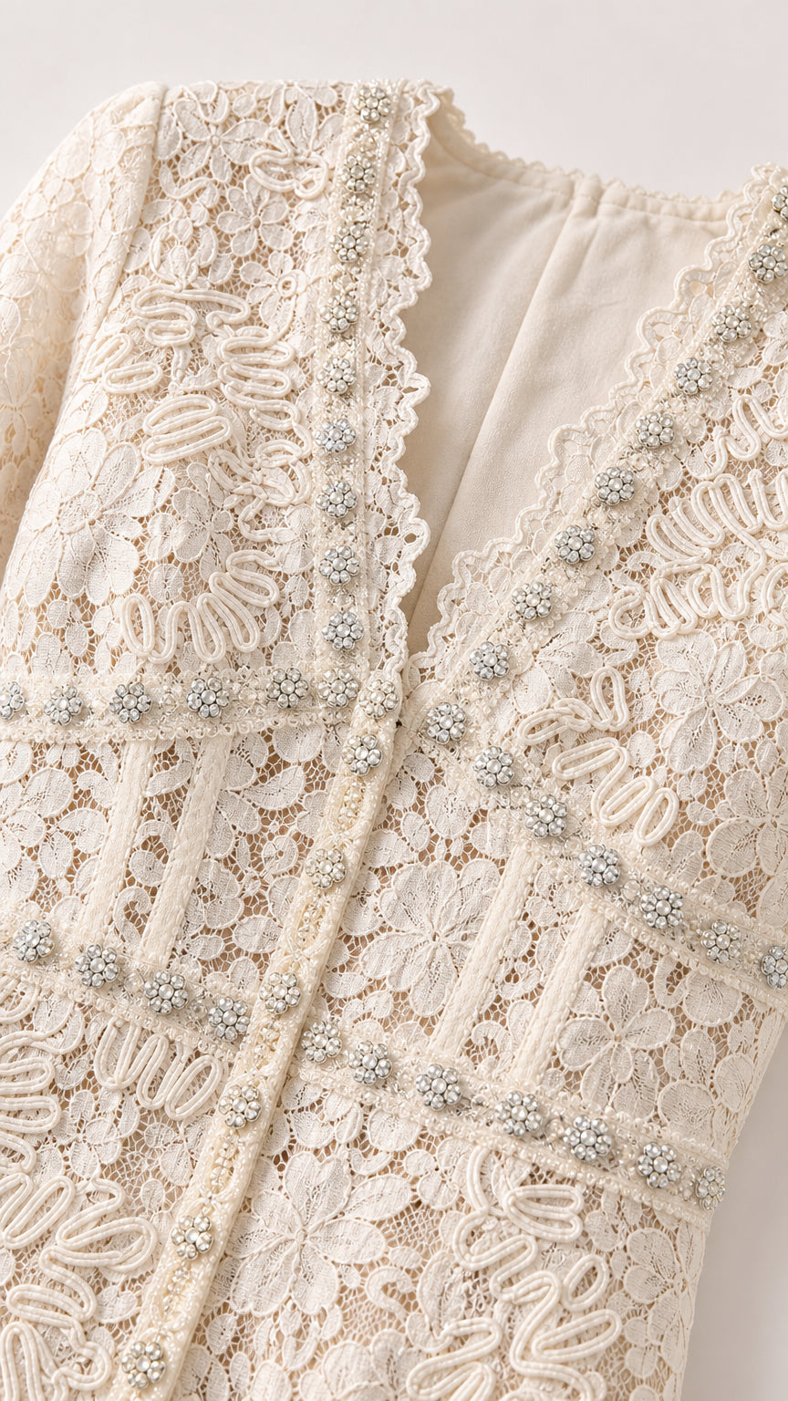 Close-up detail of textured ivory lace fabric, scalloped V-neck, and crystal bead trim